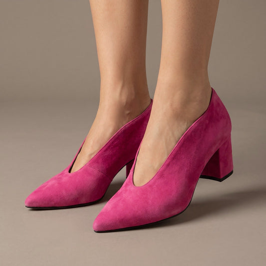 Fuchsia suede block heel pumps with a pointed toe and deep V vamp worn on bare feet